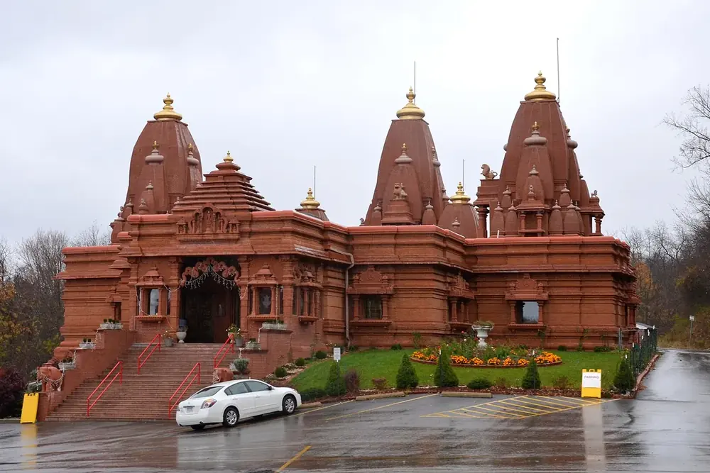 Terracotta-colored Hindu-Jain Temple with ornate spires and a flower bed in Monroeville, Pennsylvania